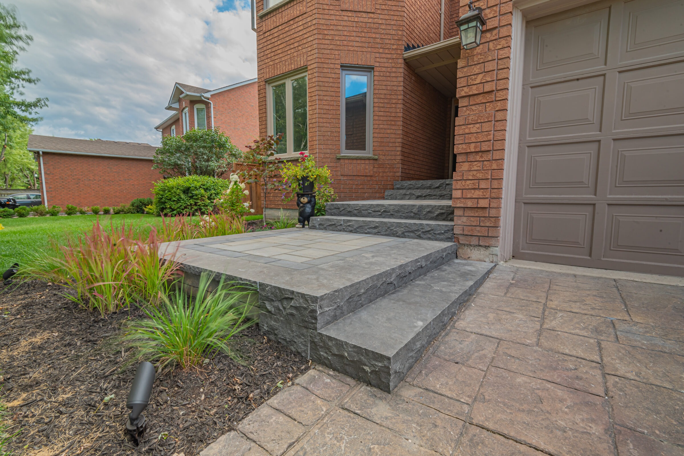 Brick house with landscaped garden, stone steps, and a decorative bear statue near the entrance. Clean design and well-maintained exterior.