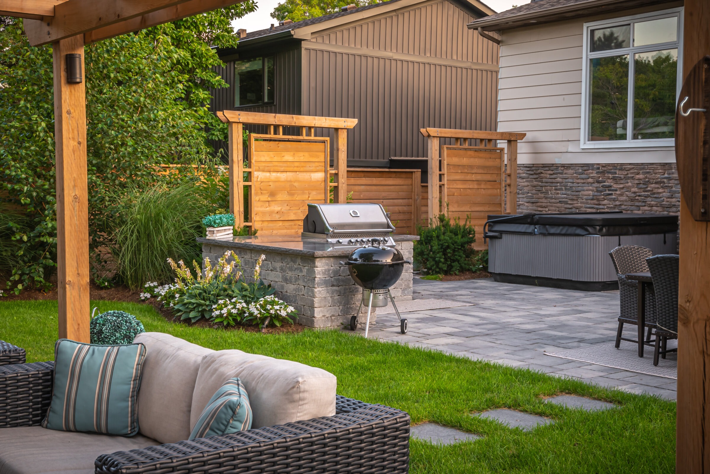 A cozy backyard features patio furniture, a grill, hot tub, plants, and wooden privacy panels, creating a relaxing outdoor living space.