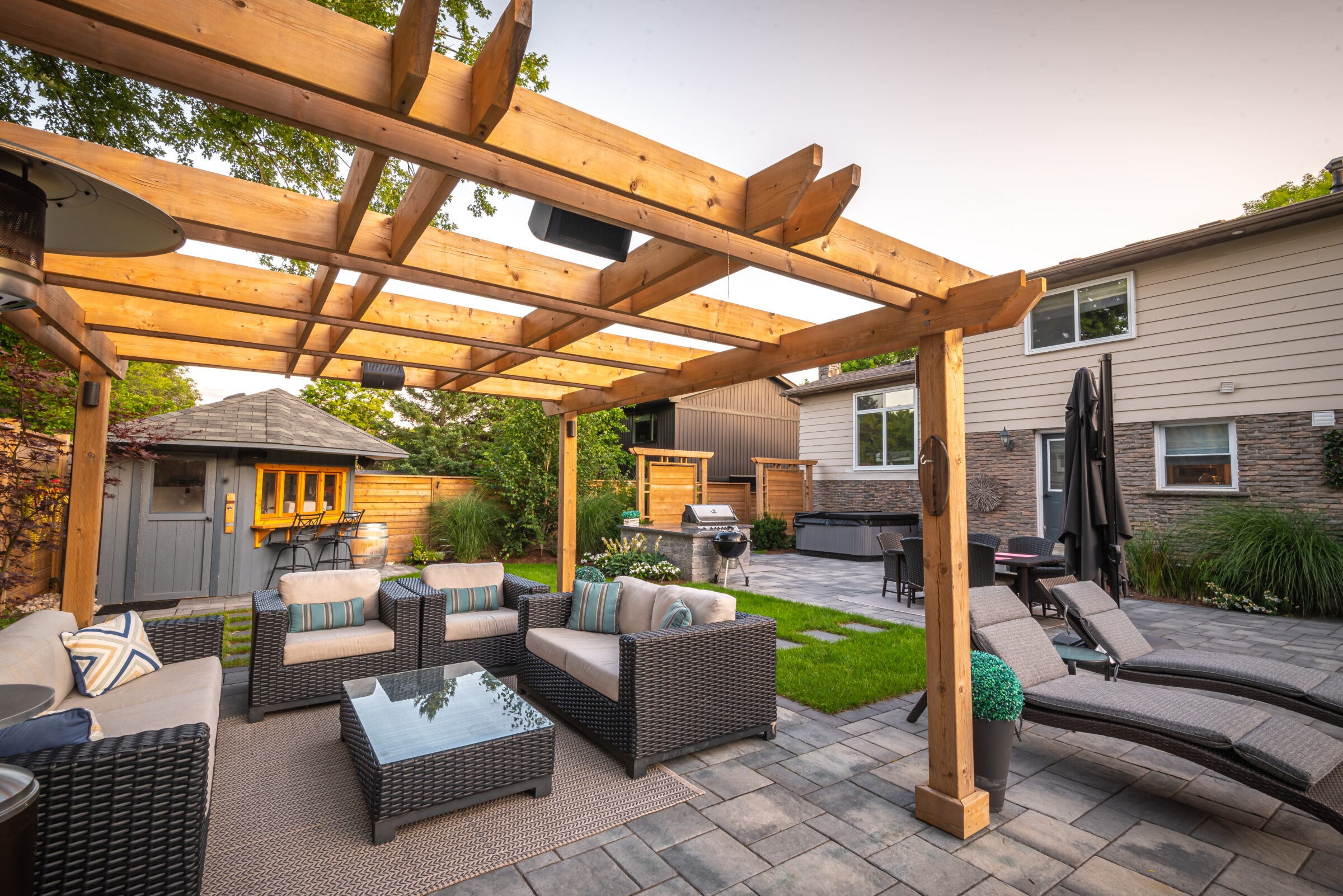 A cozy backyard with a pergola, outdoor furniture, grill, and patio surrounded by greenery and a small shed.