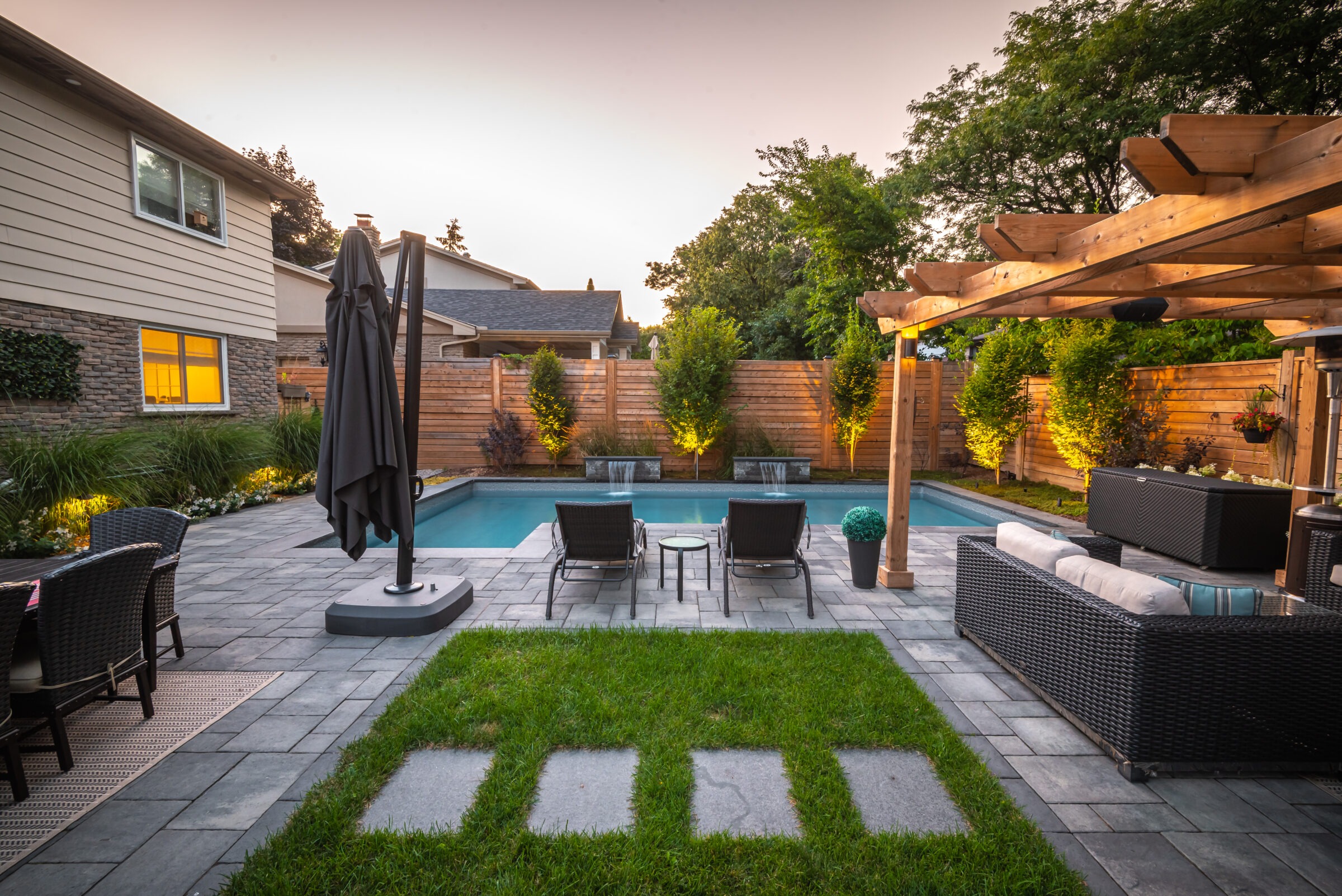 Modern backyard with a pool, lounge chairs, pergola, and greenery. Cozy outdoor seating area under soft evening light by a house.