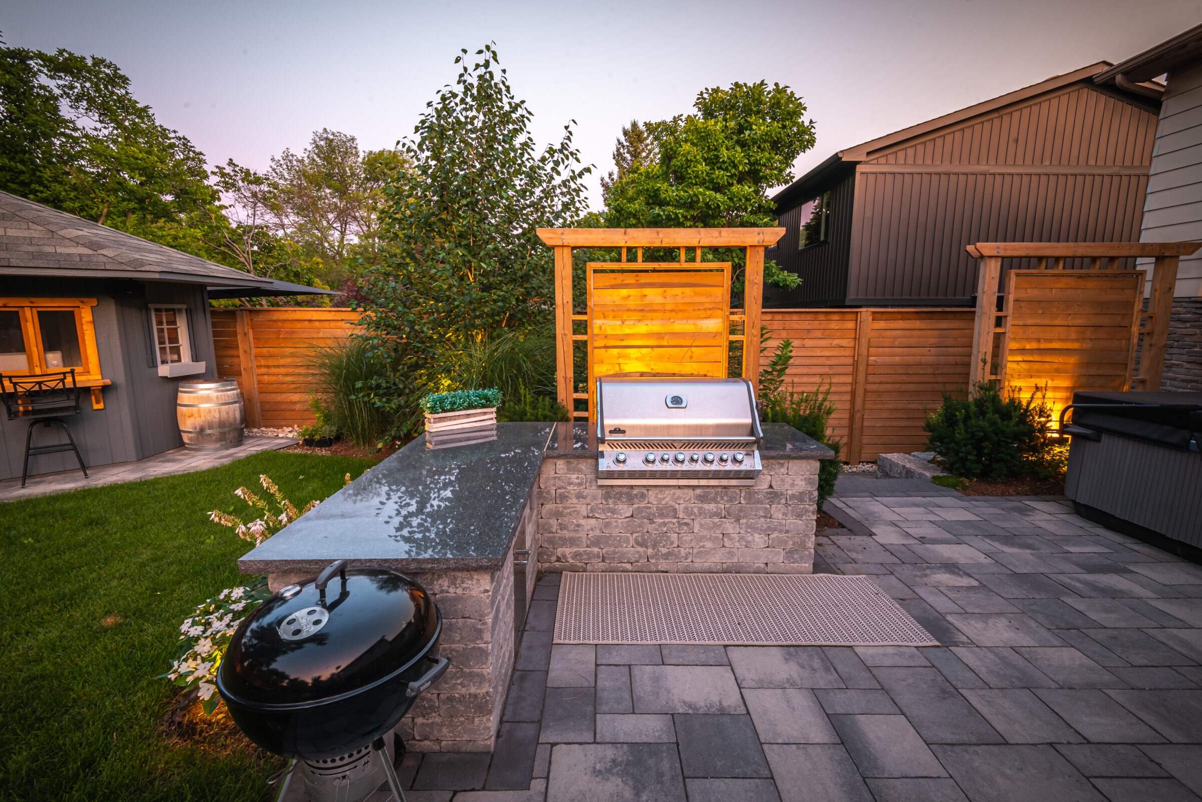 Outdoor patio features a modern grill setup, stone bar, and lush garden. Cozy shed and wooden fence complete the serene backyard ambiance.