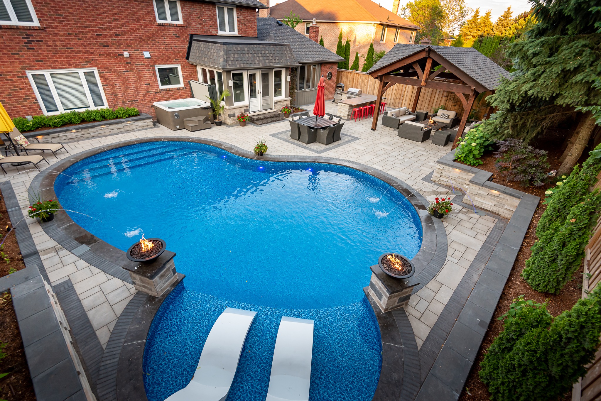 A backyard features a kidney-shaped pool, cozy seating area, outdoor dining, and a pergola, surrounded by greenery and brick houses.