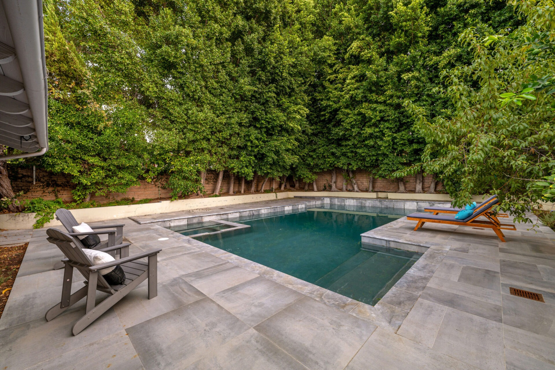 Modern backyard with a swimming pool, lounge chairs, and lush green trees